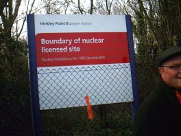 Notice reading 'Boundary of nuclear licensed site' with grinning protestor walking away from coloured strip on fence