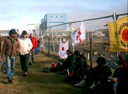 People sitting and eating picnic with backs against banner-draped fence